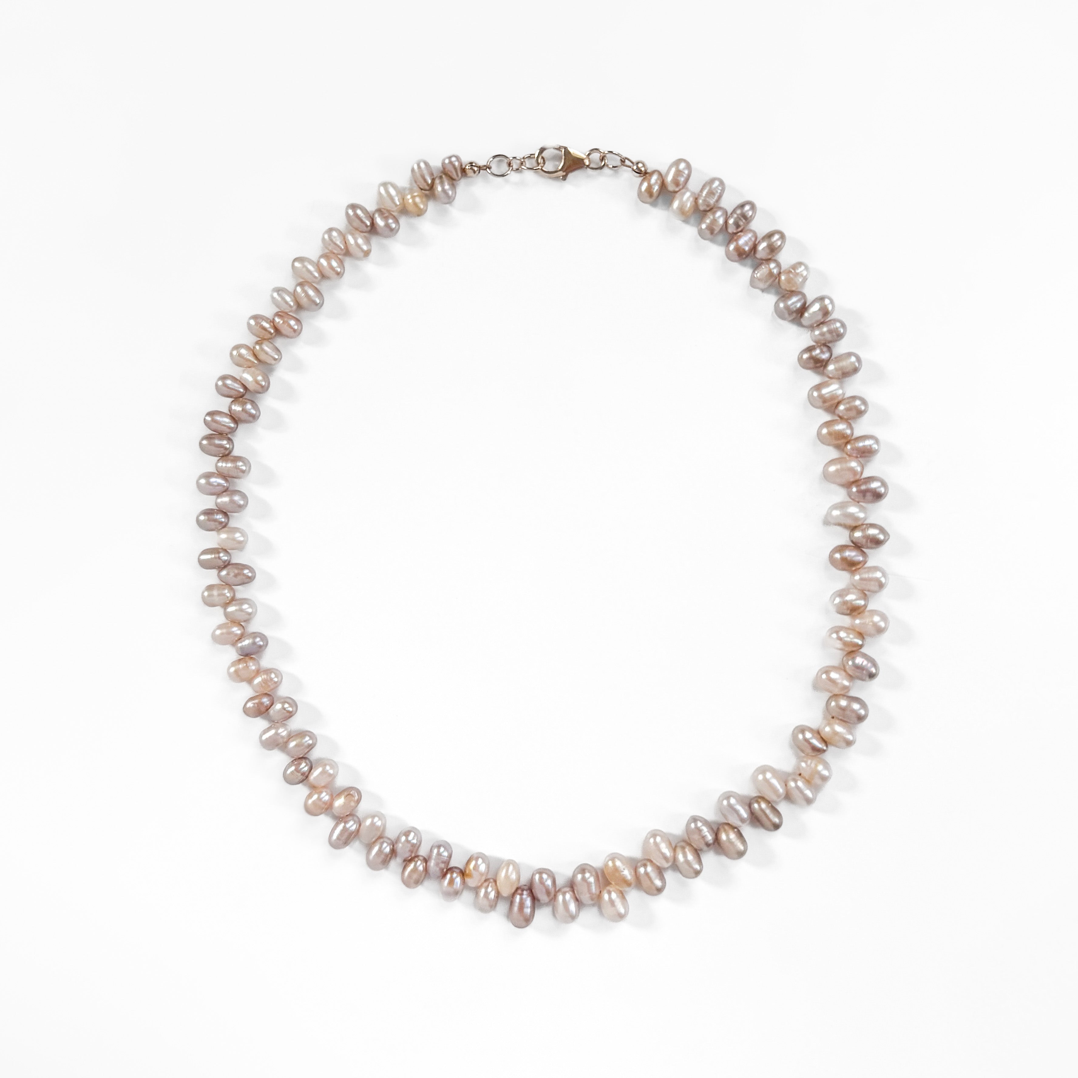 A strand of irregular baroque pearls in soft taupe, mauve, and cream tones, arranged in a circle on a clean white background.