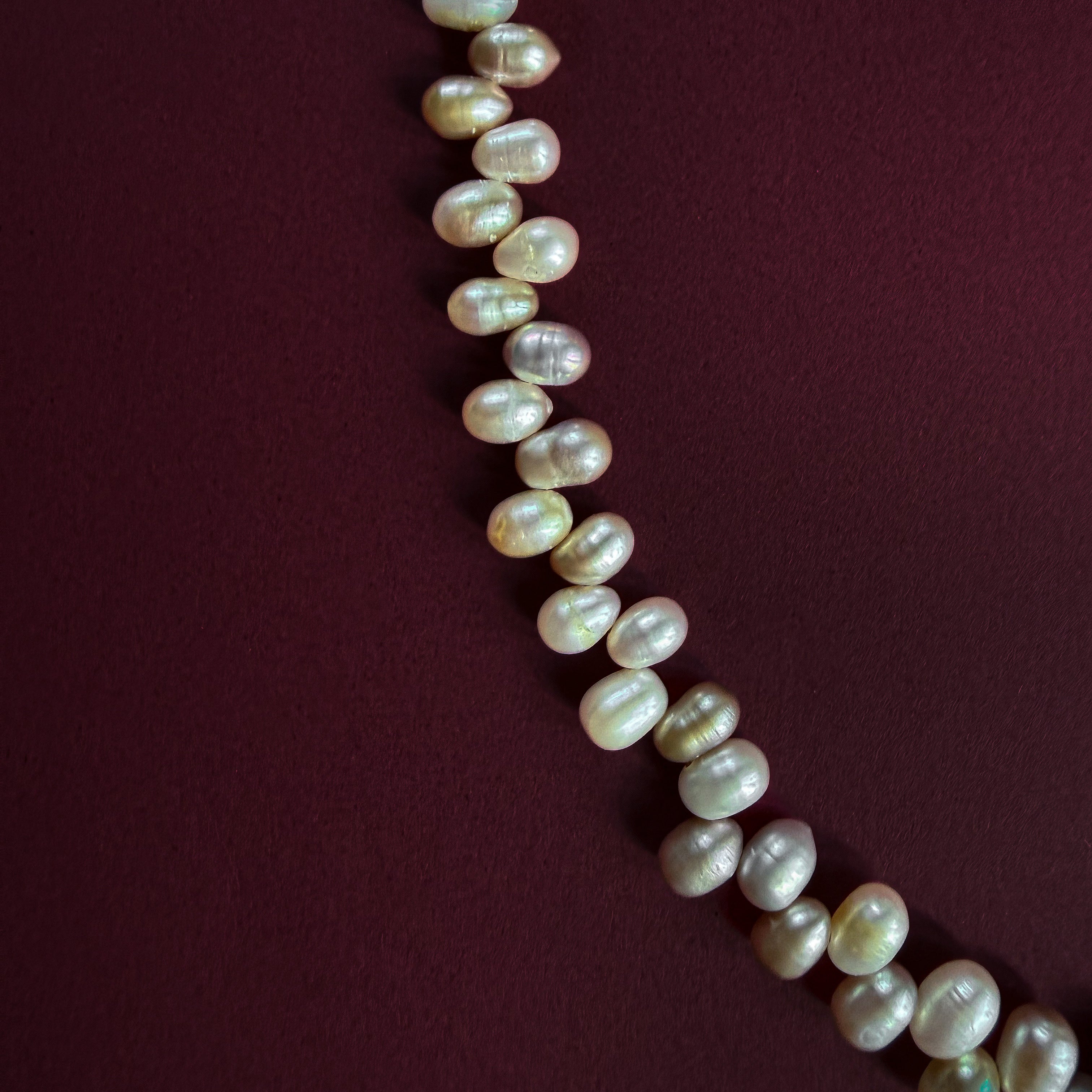 A strand of irregular, lustrous freshwater pearls arranged diagonally on a dark burgundy background.