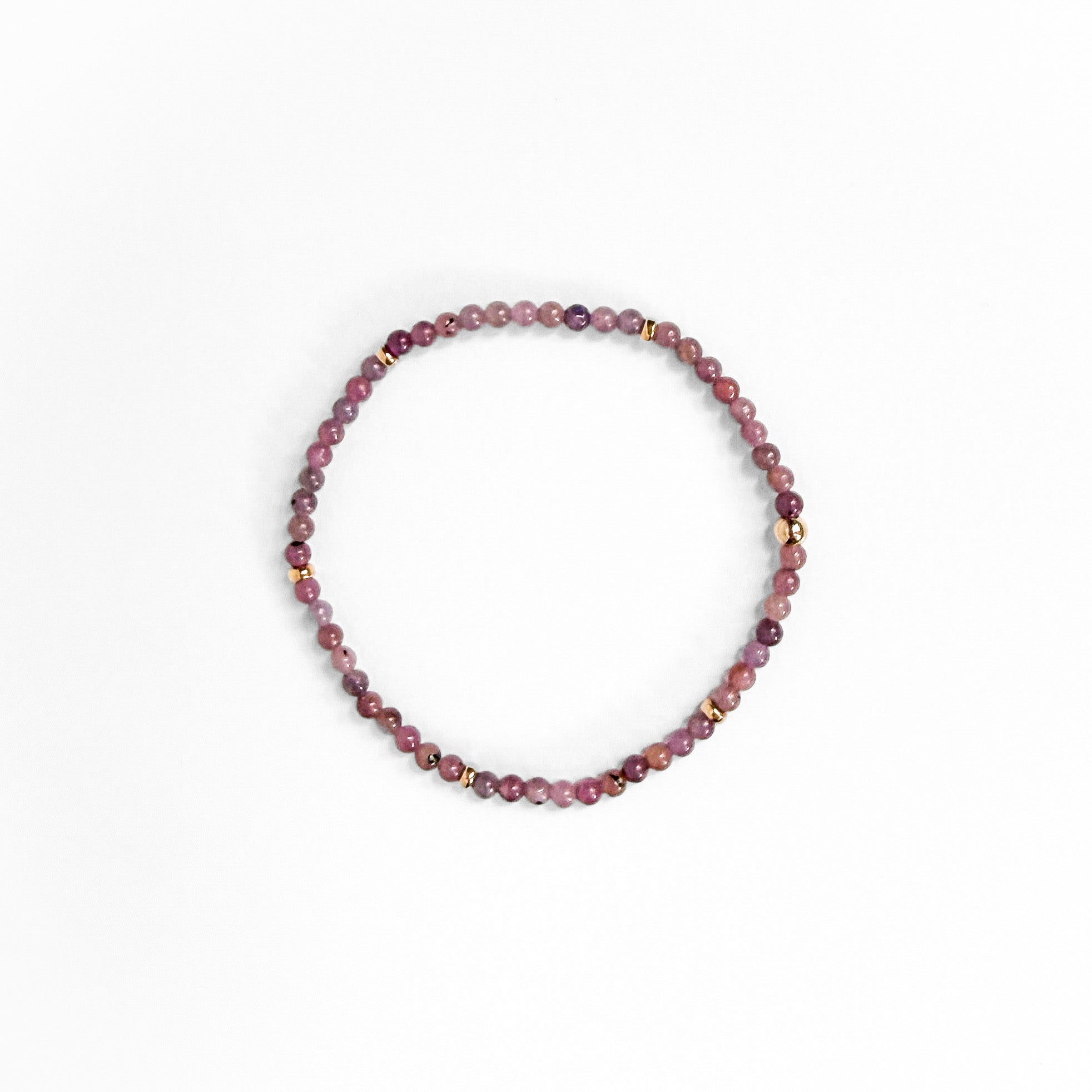 A beaded stretch bracelet made of small round beads in shades of dusty rose, mauve, and burgundy, accented with tiny gold spacer beads, shown on a plain white background.
