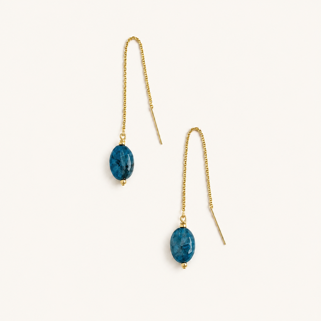 A pair of gold-tone dangle threader earrings with oval blue marbled apatite gemstone drops, shown on a clean off-white background.