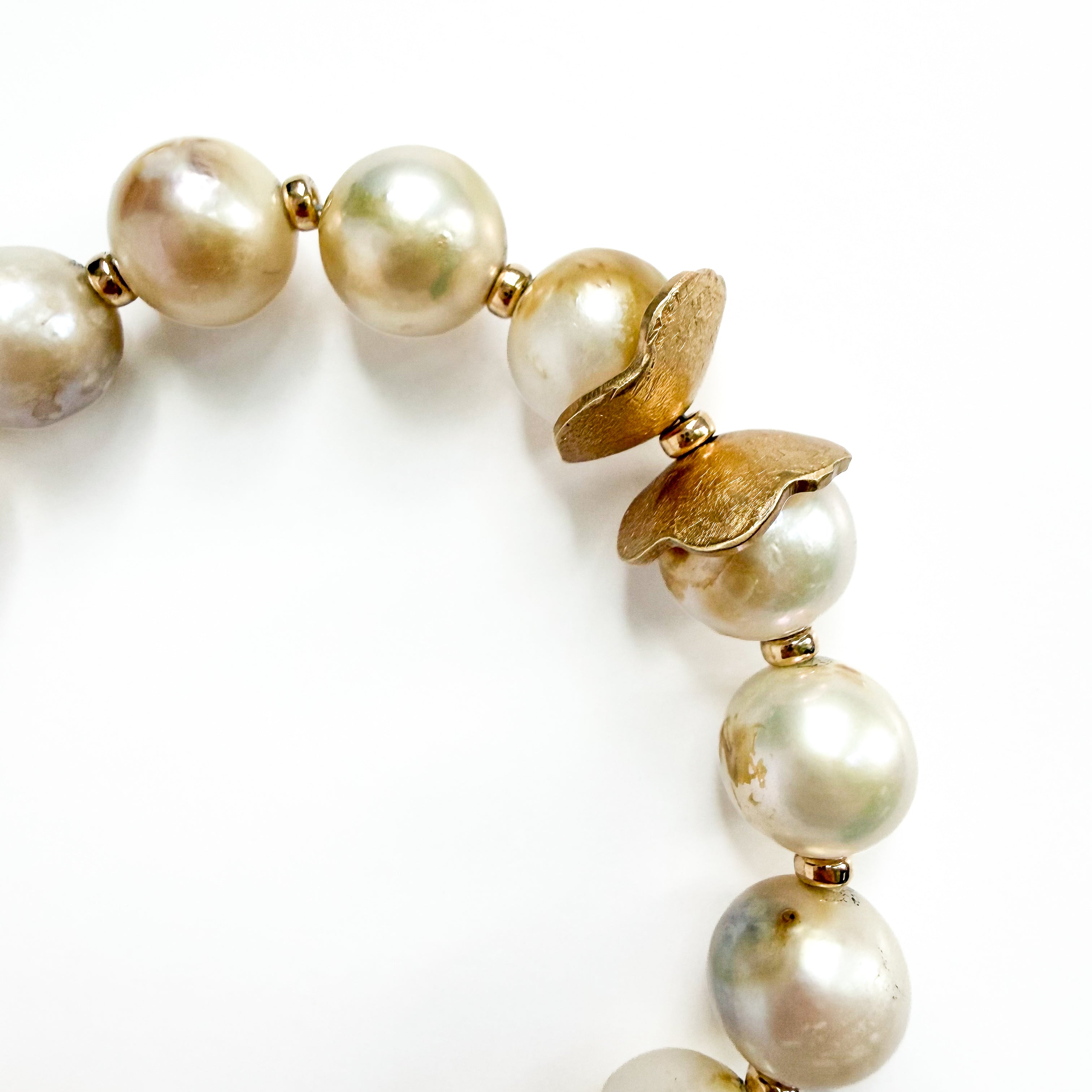 A close-up of a beaded bracelet featuring large, lustrous iridescent pearls and textured gold-toned metal flower-like spacers on a plain white background.
