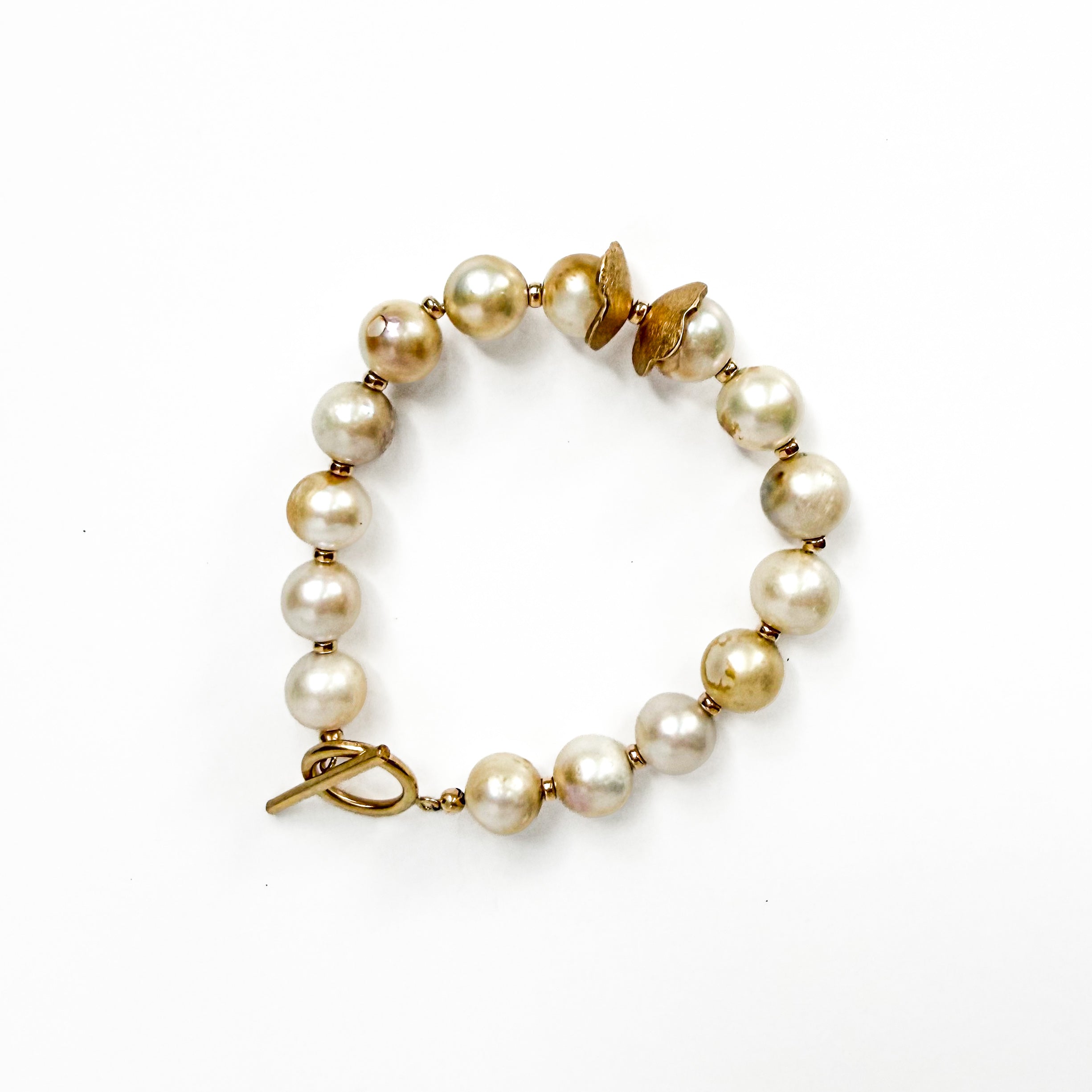 A vintage-style pearl bracelet with iridescent cream-colored pearls and gold-toned metal spacers, a butterfly charm, and a toggle clasp, shown on a plain white background.