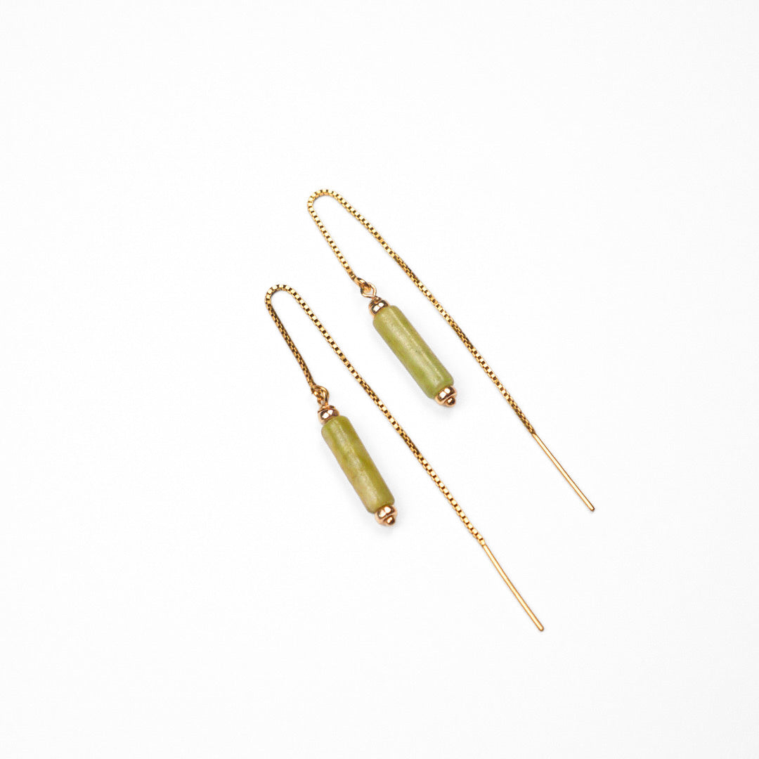 A pair of gold-toned dangle earrings with cylindrical light green beads, displayed on a clean white background.