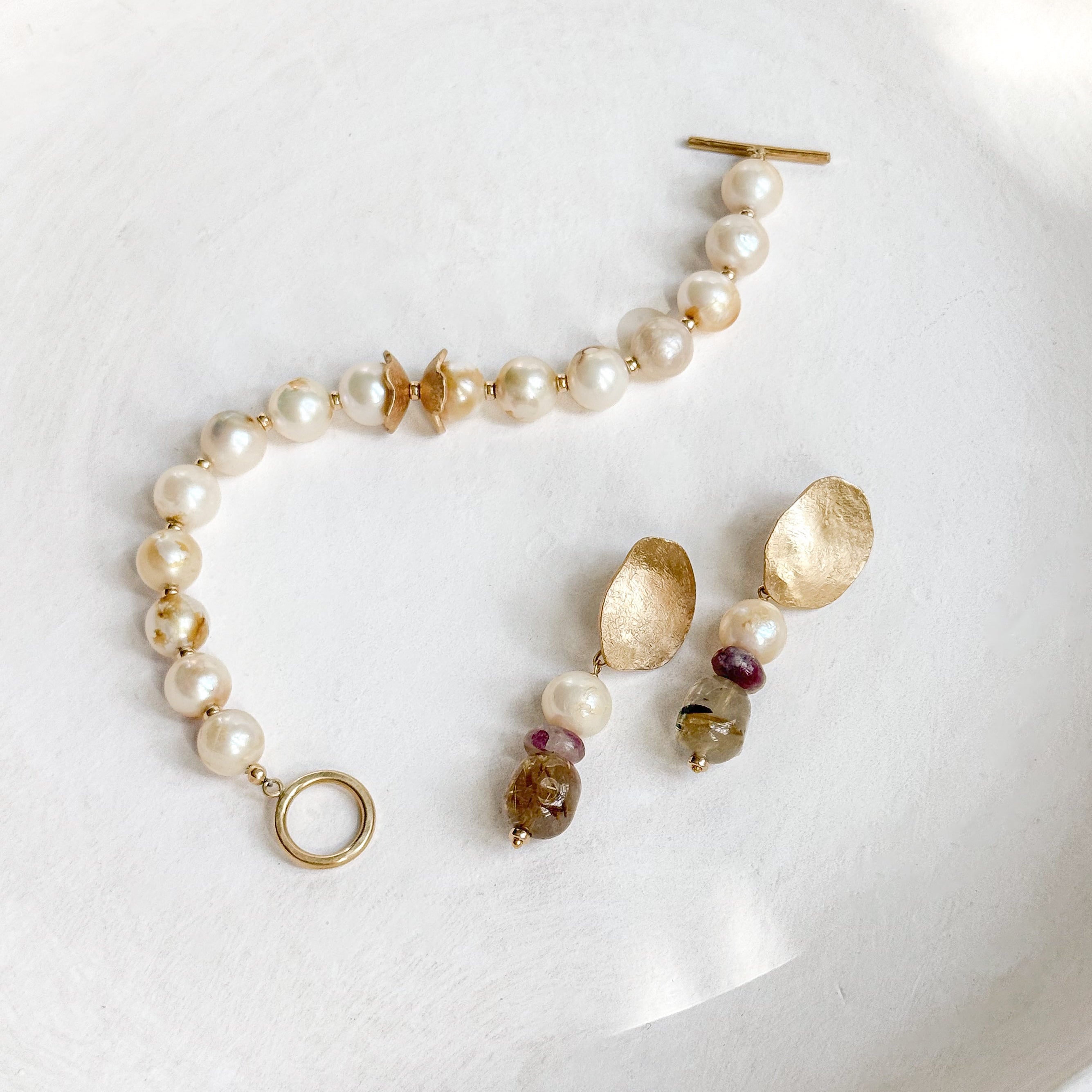 Pomona gemstone earrings with champagne pearls, tourmaline and golden rutilated quartz beside a pearl bracelet