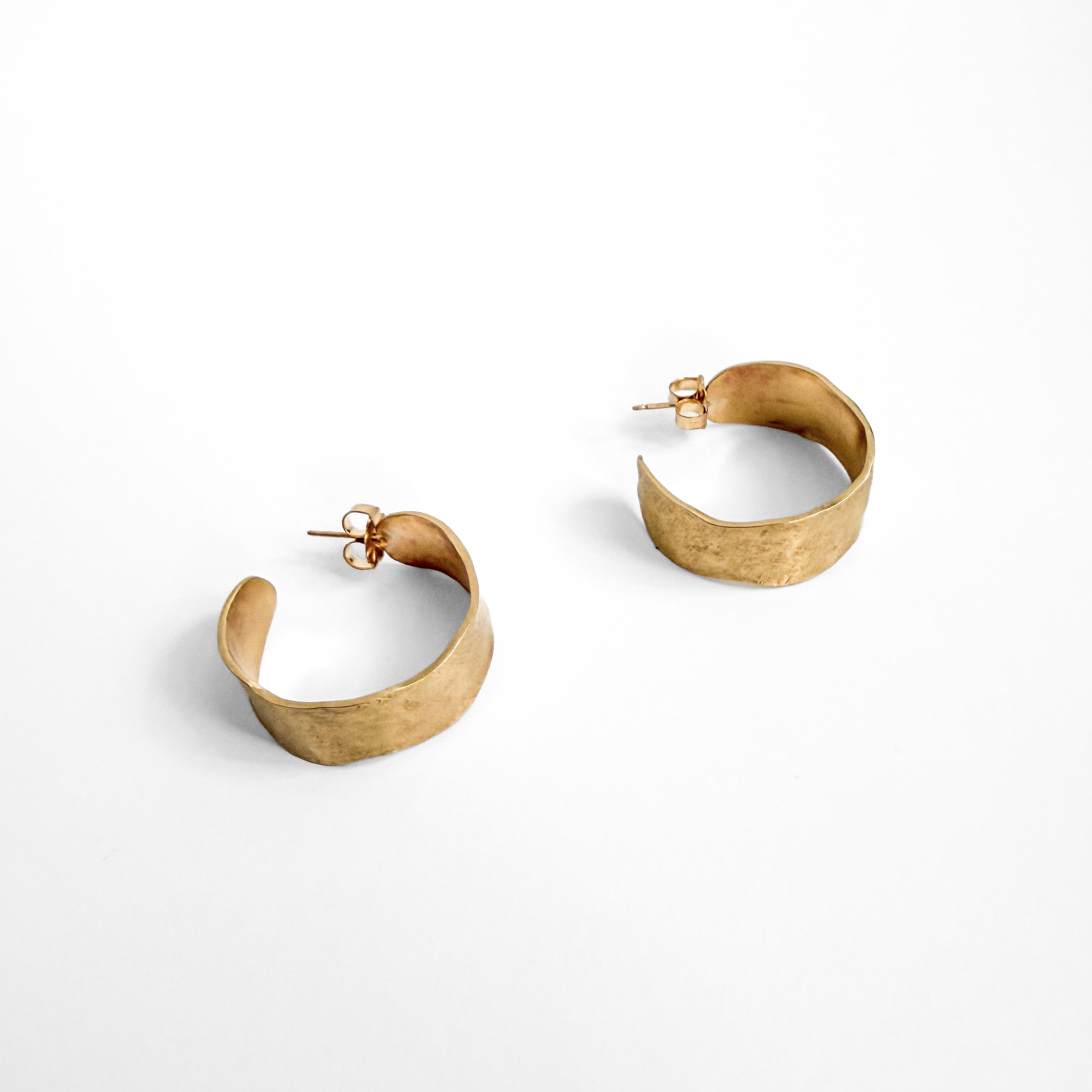 A pair of hammered gold-tone hoop earrings with a textured finish, displayed on a clean white background.